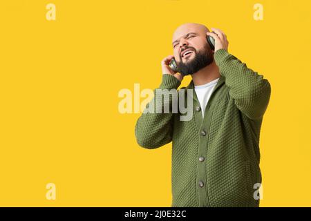 Bald man listening to music on yellow background Stock Photo