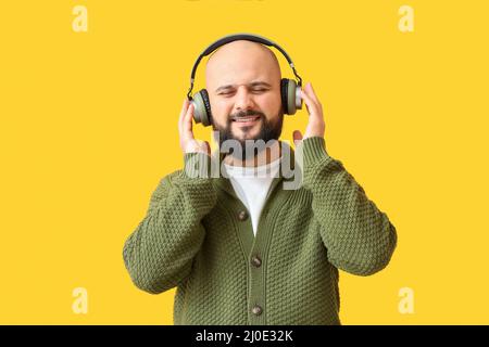 Bald man listening to music on yellow background Stock Photo