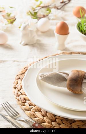 Happy Easter festive dinner with eggs, rabbit, blossom flowers on linen tablecloth. Vertical format. Close up. Stock Photo