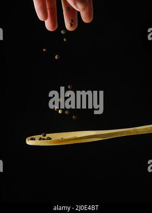 Wooden spoon and black peppercorns in frozen flight. Isolated on black background. Close-up. There are no people in the photo. Seasonings, spices. Adv Stock Photo