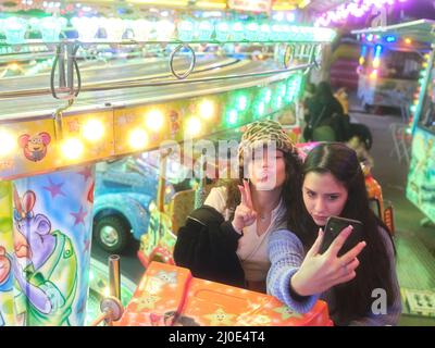 Friends sitting on a fairground ride while taking a selfie with funny expressions. Stock Photo