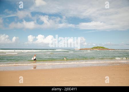 Coffs Harbour NSW Australia - 17 March 2022: Long haired elderly male surfer walking along water's edge carrying surf board on summer day Stock Photo