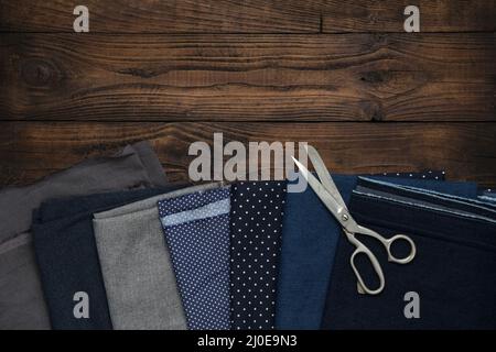Tailoring scissors and set of fabrics for sewing on wooden board. Top view, flat lay. Stock Photo