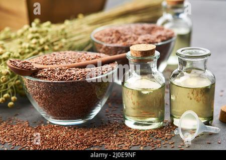 Two bottles of linseed oil and glass bowls of whole flax seeds. Bundle of linen flax plants on table. Stock Photo