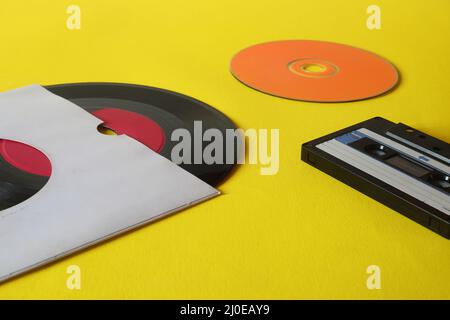 Musical storage devices and copy space. Old audio cassette tapes, compact disc and vinyl record on yellow background with text space. Stock Photo