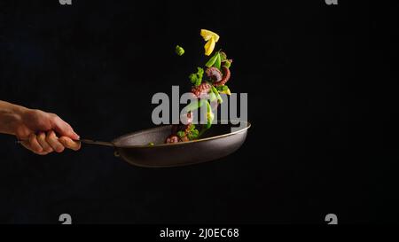Asian cuisine dish. Octopuses with lemon slices and vegetables in a pan in frozen flight on a black background. Seafood recipes, gourmet food. Cookboo Stock Photo