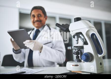 Medical research that makes a difference. Shot of a microscope on a laboratory table with a scientist using a digital tablet in the background.