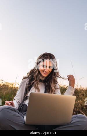 Young woman with a backpack on, using a laptop to charge his smartphone. Teleworking. Digital nomad. Copy space Stock Photo