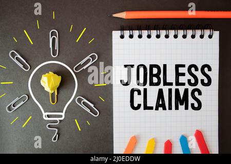 Jobless claims text on white paper from a notepad on a wooden background. wooden blocks magnifier Stock Photo