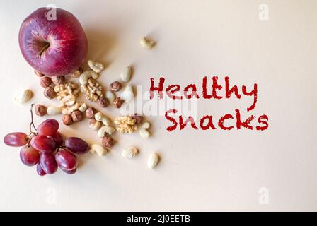 Healthy natural, organic snacks, various nuts, like walnuts, cashews, hazelnuts and almonds, grapes and apples isolated on beige background Stock Photo