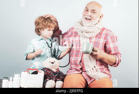 Kid doctor stethoscope examine patient. Little doctor. Grandfather and kid playing clinic. Smiling little boy playing doctor and listening old Stock Photo
