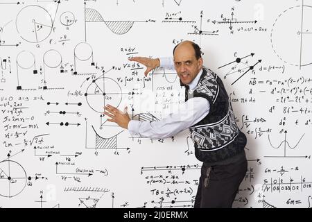 Middle aged caucasian mathematician explaining mathematical equations on a white wall Stock Photo