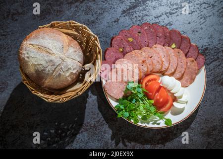 Slicing different types of sausages on a plate with herbs and vegetables Stock Photo