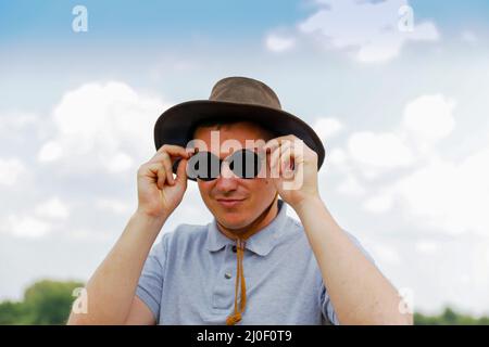 Male wearing black sunglasses. Portrait of farmer with blue sky in background. Young man wearing sunglasses and cowboy hat in field. Closeup. Happy Stock Photo