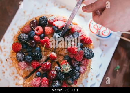 Female hand cuts a raspberries blackberry birthday cake with candles number 30 on defocused background. Selective focus macro sh Stock Photo