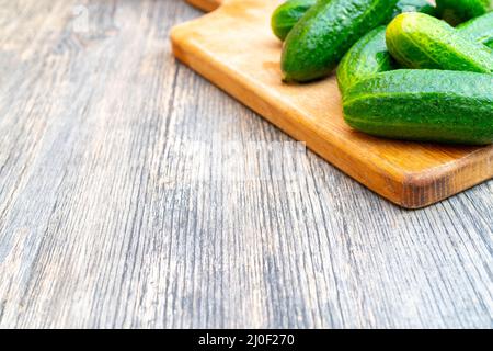 Ripe green cucumbers on cutting board for vegetables. Vegetables on kitchen table. Stock Photo