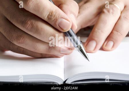 The right hand of a man writing with a pen on a notebook with blank pages. Stock Photo