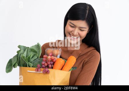 Happy Asian woman is smiling and carries a shopping paper bag after the courier from the grocery came to deliver his goods at home. Concept of Superma Stock Photo