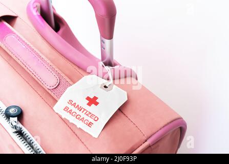 A red suitcase with a paper tag indicating that the baggage has been sanitized. Stock Photo