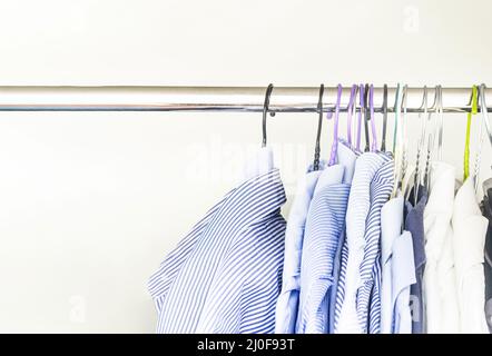 A group of men's shirts of various colors hung with hangers inside a wardrobe Stock Photo