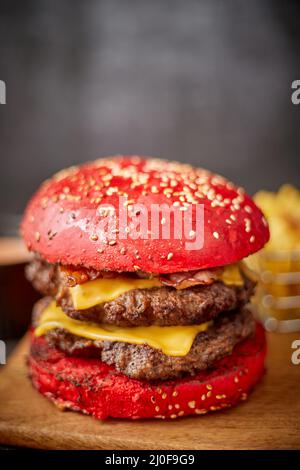 Homemade red sesame bun double bacon cheese burger. Served with french fries on wooden board. Stock Photo