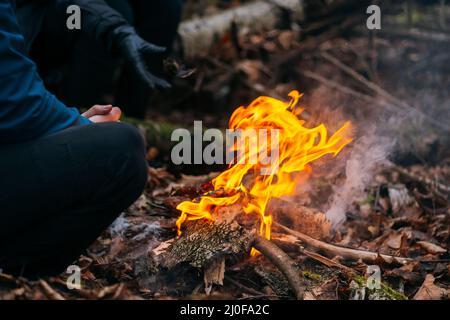 Man warms his hands on fire. Burning wood at evening in the forest. Campfire at touristic camp at nature. Barbeque and cooking o Stock Photo