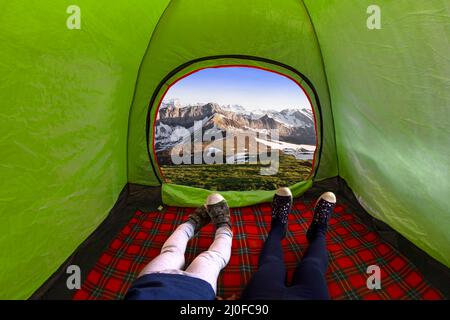 Two kids inside on a camping tent looking at the mountains during the day Stock Photo