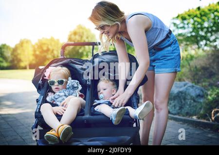 Strapped in for a stroll in the park. Shot of a young woman putting her daughters into a pram on a day outdoors. Stock Photo