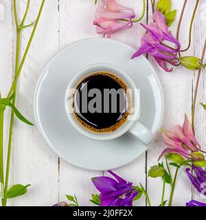 A Cup of black coffee on a saucer and flowers on a white table top view close-up flat lay Stock Photo