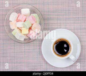 A Cup of black coffee on a saucer and marshmallows on a pink napkin background, top view flat lay Stock Photo
