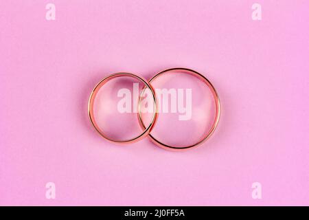 A pair of gold wedding rings on a pink background, top view flat lay Stock Photo