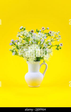 Beautiful bouquet of wild flowers chamomile and clematis in a white jug on a yellow background close Stock Photo