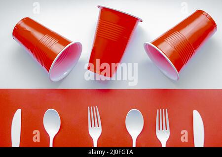 Single use white plastic cutlery and red plastic glass on a red and white background. Concept: Ban single use plastic Stock Photo