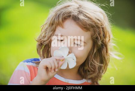 Funny child smelling plumeria flower, face close up. Kids in summer nature park, portrait. Stock Photo