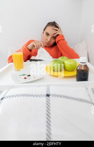 A young teenager lies on a bed and takes out handkerchiefs to blow her nose. Stock Photo