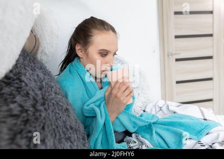 A young teenager drinks hot tea with herbs while lying on her bed under the covers. Stock Photo