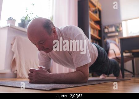 Cheerful senior hispanic man doing a side plank exercise at living room. Doing yoga at home Stock Photo