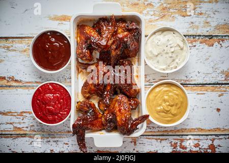 Chicken wings in thick barbecue sauce with various side dips. Served on white cast iron dish Stock Photo