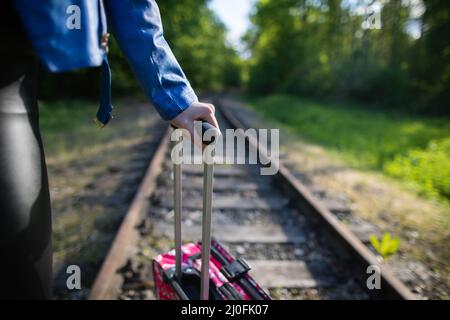 A close-up view of a teenage girl holding a pink travel bag by a retractable plastic handle while walking along the railroad tra Stock Photo