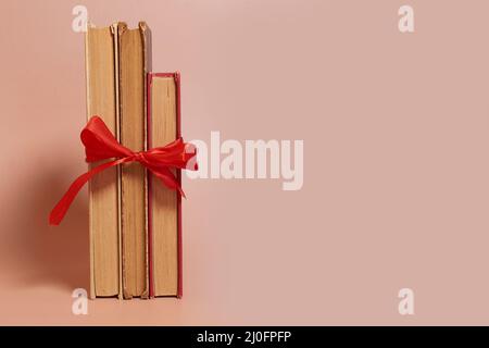A stack of old worn books tied with a red ribbon on a colored background Stock Photo