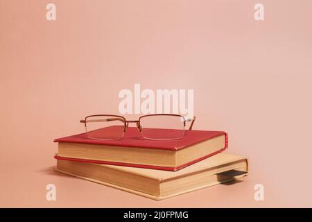 Reading glasses lie on a stack of old worn books on a colored background Stock Photo