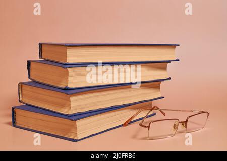Reading glasses lie next to a stack of books on a colored background. Side view Stock Photo