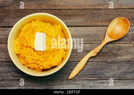 Pumpkin rice porridge with milk and a piece of butter and a wooden spoon on a wooden background top Stock Photo