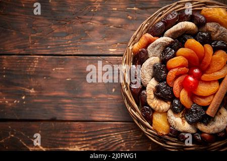 Mix of dried fruits in a small wicker basket on wooden table Stock Photo