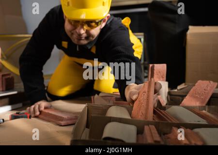 The construction worker reaches for another brick-shaped decorative tile to continue with the planned work. Construction worker Stock Photo