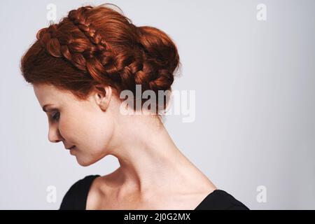 Soft and romantic. Studio shot of a beautiful redhead woman with a braided up-do posing against a gray background. Stock Photo