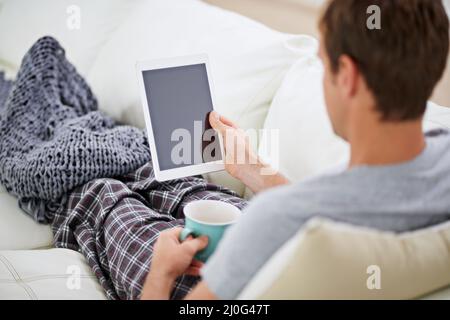 Enjoying the perks of wireless technology. Shot of a man in pajamas having coffee while using his digital tablet. Stock Photo