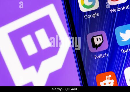 The icon of the Twitch live streaming service application among other applications on the smartphone screen. On the background is the Twitch logo. Stock Photo