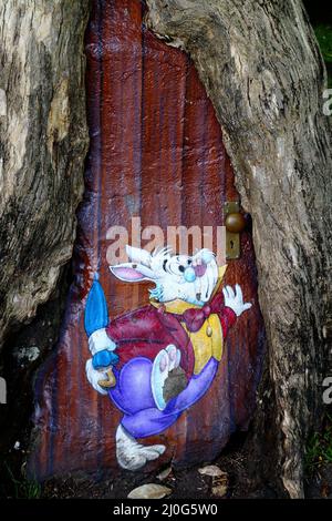 Alice In Wonderland White Rabbit and a door painted on a tree trunk Stock Photo