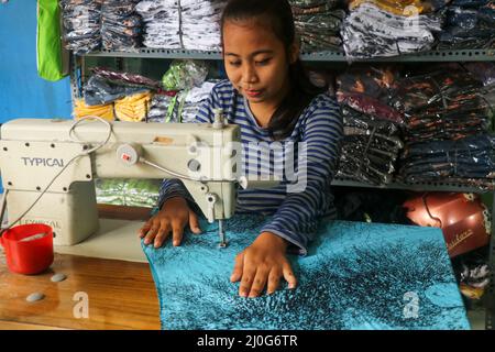 Asian dressmaker woman sews clothes on sewing machine. Smiling in process seamstress in workshop. Young tailor seamstress working on textile factory Stock Photo
